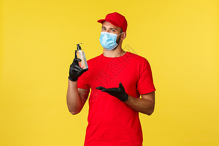 Covid19 送货订单 购物 无接触处理和社会疏离概念 穿红色制服和T恤衫的英俊信使带着手套的医疗面具引入新的洗手剂工人口罩快图片