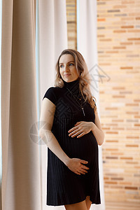 深思熟虑的孕妇抚摸她的肚子成人家庭父母母亲母性房间生活妈妈怀孕窗户图片