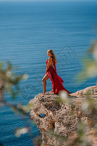 一个穿着红色飞行服的女人 在大海的背景下 飘在风中发抖着尾巴海滩女孩幸福女士丝绸日落天空衣服海洋图片