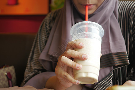 在咖啡馆喝香蕉奶昔的年轻妇女牛奶白色饮料香蕉女性眼镜奶制品液体奶油背景图片
