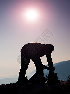 专业摄影师正把相机装进岩石高峰的背包中 梦雾般的风景 在美丽的山谷中春橙色粉色薄雾日出图片