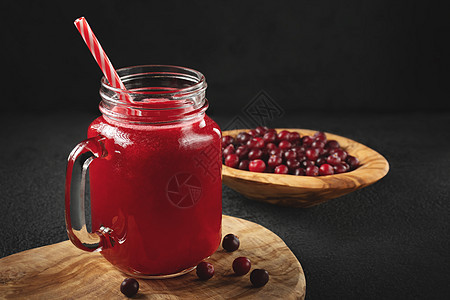 在一个玻璃罐子里用黑桌上的稻草来愈合红莓汁 健康饮食概念图片