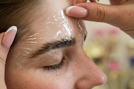 师傅在眉毛涂层时用塑料胶片沙龙女孩建筑学绘画眼睛治疗温泉睫毛造型师磨练图片