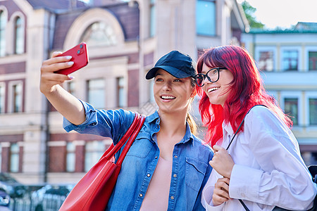 两个美丽的少女 玩得开心 在智能手机上拍自拍肖像相机城市女性朋友们青春期幸福照片电话享受快乐图片