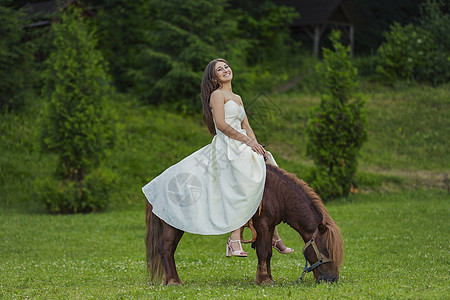 穿着白裙子的女孩骑着小马农村运动马背微笑友谊孩子农场帽子骑术牧场图片