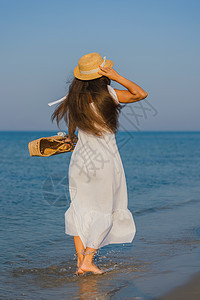 在沙滩上戴帽子的女人柳条天空蓝色享受海洋棕褐色闲暇女性地平线金发女郎图片