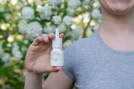 快乐的女人展示鼻涕喷洒 在一棵开花的树的背景天气喷嚏香味女性示范花粉症状鼻子鼻孔药品图片