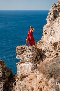 一个穿着红色飞行服的女人 在大海的背景下 飘在风中发抖着太阳天空丝绸幸福女士衣服日落成人海滩女孩图片