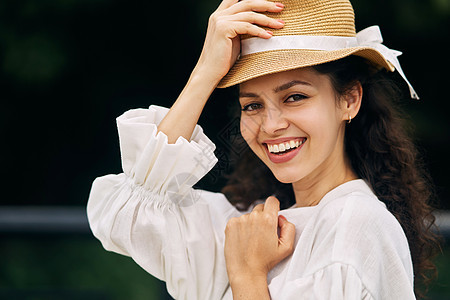 在夏日公园戴帽子的年轻美女草帽假期日光女性成人幸福微笑摄影衣服享受图片