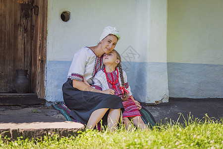 母亲和女儿坐在房子附近 穿着乌克兰民俗服装的乌克兰人旅行耳环妈妈微笑家庭衬衫组织帽子汽艇手工图片