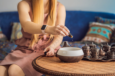 妇女在桌上的芳香扩散器中添加必要的石油薄雾香水康复化妆品净化器瓶子温泉除臭剂女士蒸汽图片