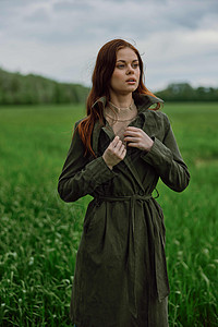 一位美丽的女士站在绿地上 调整她的大衣图片