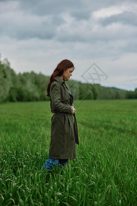 一个穿着长长雨衣的女人 站在高草绿草地上 在春天的雨季里摄影风光模特下雨愿望裙子大衣女性场地农田图片