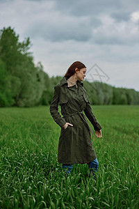 一个穿着长长雨衣的女人 站在高草绿草地上 在春天的雨季里下雨模特风光愿望大衣活动田园女性场地农田图片