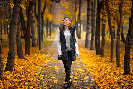 一位年轻女子在秋天的公园中散步 沿巷子走着秋叶落叶图片