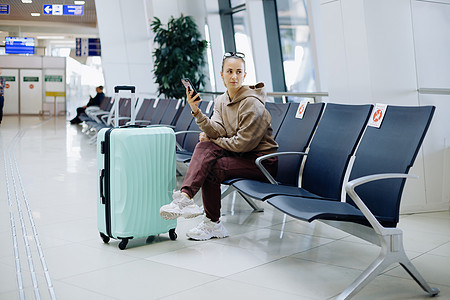 的年轻女子在机场使用她的智能手机乘客车站女性案件享受旅游游客玻璃电话大厅图片