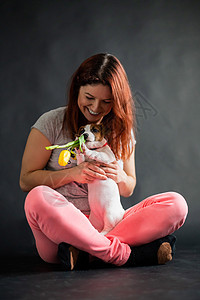 红头发女人拿着黄色的郁金香 带着她的小狗在黑人背景下玩耍工作室情感幸福犬类宠物猎犬女孩拥抱快乐友谊图片