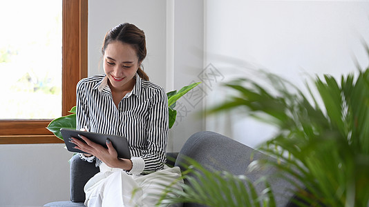 在沙发上和在互联网数字平板电脑上冲浪的千百年富丽堂皇的女人图片