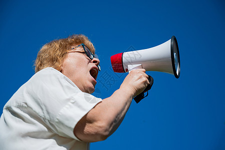 情绪激动的高级女性在外面用扩音器发表演讲 一位领取养老金的人对着蓝色背景的扩音器大喊大叫 集会的女领袖用扩音器说出情况政治广告发图片