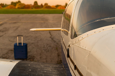 一个蓝色手提箱和一架停放的小型私人飞机 日落时带螺旋桨的四翼飞机用于空中出租车 自我旅行的概念 VIP 人员的飞机飞机场航天跑道图片