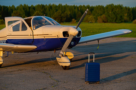一个蓝色手提箱和一架降落的小型私人飞机 带螺旋桨的四人座飞机 用于空中出租车 自我旅行的概念 VIP 人士的飞机飞行员航班探索民图片