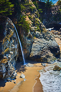 小瀑布从沿海岩石倾泻到沙滩上图片