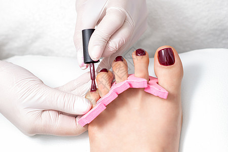 修甲师傅在画女性脚趾甲分隔器身体栗色治疗服务修脚手套趾甲沙龙搪瓷图片
