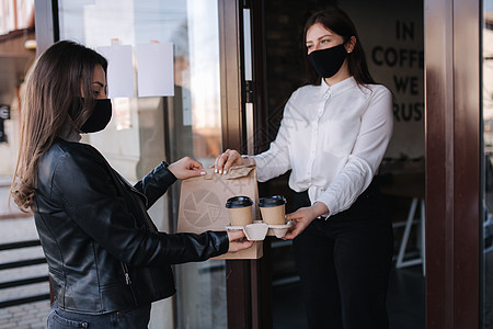 年轻女子戴着面具站在户外 在咖啡馆里使用 NFC 技术通过智能手机支付账单 女性顾客使用非接触式技术付款 女人按顺序服用 带走食图片