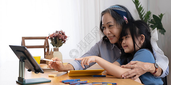 慈爱的老祖母拥抱小女孩孙子的肩膀 协助准备家庭作业 提供建议 友好的老妇老师看着小学生写数学题的解决方案老太婆故事老年金发小姑娘图片