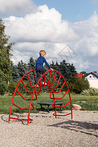 一个非常勇敢的小男孩在操场上爬上一个红色的金属大拱形梯子 儿童游戏中父母关爱和安全的概念闲暇假期学习运动托儿所活动公园男性训练体背景图片