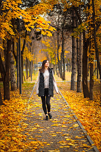 一位年轻女子在秋天的公园里走着一条小巷边的小巷图片