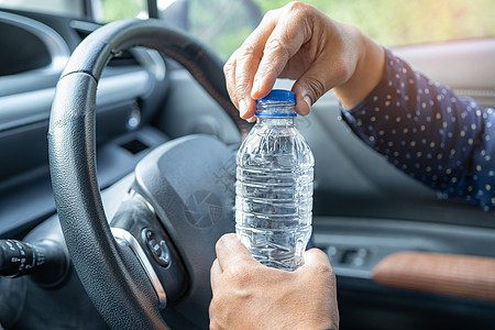 亚洲女司机在开车时拿着瓶子饮水 塑料热水瓶引起火灾 在汽车驾驶期间安全天空车辆成人速度奢华发动机女士车速危险图片