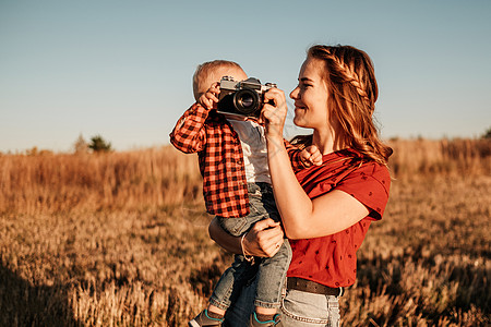 快乐的妈妈和她的小儿子在阳光明媚的日落时分在城外的田野里享受夏日周末蓝色儿子女性孩子乐趣男生相机家庭公园衣服图片