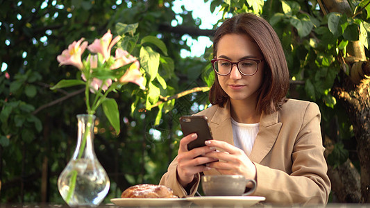 一位年轻的女商务人士坐在咖啡厅里 在电话上发短信图片