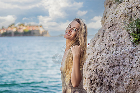 圣史蒂芬岛美景背景的女性游客 黑山布德瓦里维埃拉的海滩假期幸福天线半岛蓝色天空日落裙子女士图片