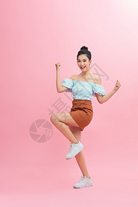 一位兴奋的亚洲女性跳跃和看镜头的肖像 在粉红背景上被孤立粉色女士运动顾客乐趣微笑裙子女孩喜悦情感图片
