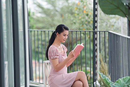 美丽的年轻女子在阳台上读一本书假期快乐小说文学寒意公寓学生闲暇女士阅读图片