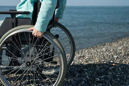 白种女人坐在海边的轮椅上 手紧一点机动性海洋女性药品事故享受海岸游客减值麻痹图片