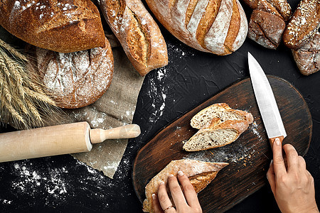 女人用手在生锈的木板上切面包 上面有小麦耳朵和刀子糕点午餐饮食面粉女性产品高架食物背景种子图片