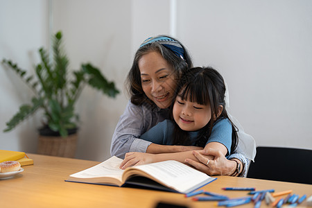 特写微笑的成熟祖母给小孙女看书 讲有趣的童话故事 爱老妇人拥抱漂亮的学龄前女孩 在家里舒适的沙发上放松背景图片