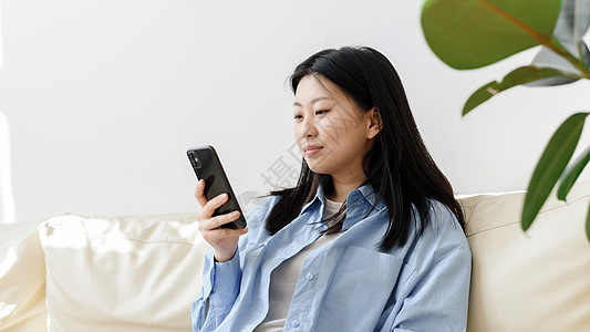 年轻的亚洲女性在客厅的沙发上放松 用智能手机浏览新闻 韩国女士在现代手机上写信息 通过网站在线购物 网页横幅图片