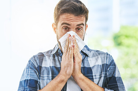 看来又是流感季节了 白天 一个看起来不舒服的年轻人在建筑物内用纸巾擤鼻涕的画像图片