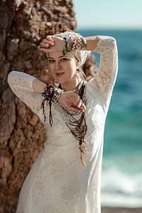 中年妇女穿着金发 穿白色长裙 在海滩上装饰着她的颈部和手臂的衣物女士支撑海洋天空荒野配件成人婚礼女孩裙子图片