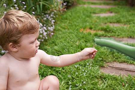 享受各种感觉-童年发展 可爱的幼儿被花园里的水罐所迷惑 (笑声)图片