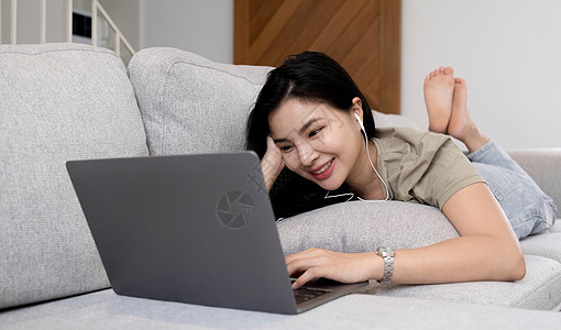 社交媒体时间与她的平板电脑保持联系一位开朗的女士躺在沙发上 在客厅里使用家里的平板电脑 沙发上拿着平板电脑微笑的女人移动阅读应用图片