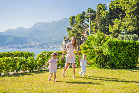 夏日 快乐的年轻母亲和两个小孩 男孩和女孩在绿色公园里玩接球游戏 童年 为人父母 幸福的概念女性草地成人男生女儿孩子女士微笑跑步图片