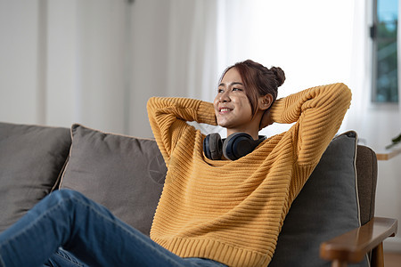 戴着耳机 笑得开心的亚洲年轻女性在家里的沙发上听音乐 人和休闲概念电话闲暇房子乐趣技术享受歌曲女孩长椅成人图片