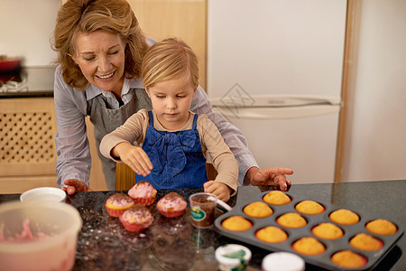 蛋糕老板在工作 一个小女孩在祖母的帮助下装饰纸杯蛋糕图片