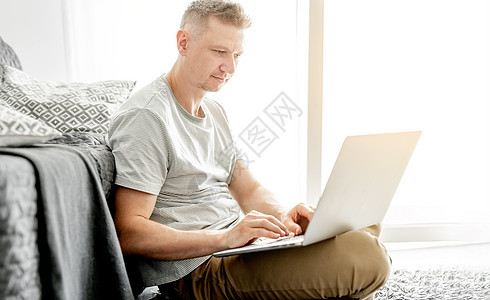 英俊的年轻人在笔记本电脑上工作自由职业者男性成人技术沙发客厅枕头办公工作者男人图片