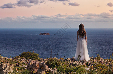 穿着白色婚纱的新娘 站在悬崖边缘看着大海图片
